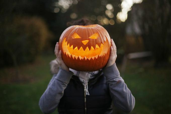 o fată care ține în fața capului un dovleac de Halloween sculptat și iluminat