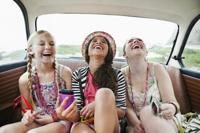 trei fete râzând pe bancheta din spate a unui vehicul