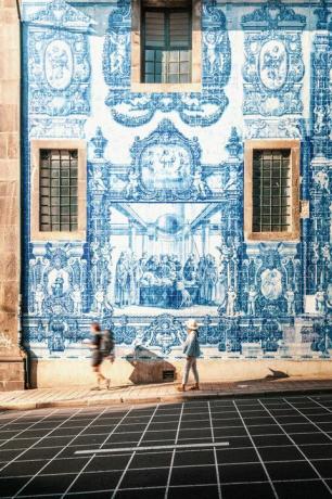 femeie care merge în porto pe peretele de țiglă azulejos albastru și alb al bisericii capela das almas din porto