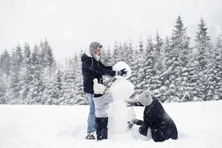 familie de trei oameni care construiesc un om de zăpadă în zăpadă