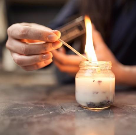 Cultură femeie anonimă cu chibritul aprins aprinzând lumânare aromată într-un borcan de sticlă așezat pe masa de marmură acasă