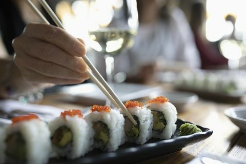 Femeie cu betisoare care ajunge la sushi pe tava restaurantului