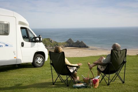 Un cuplu cu un picnic relaxându-se pe scaunele de lângă autovehiculul lor, bucurându-se de priveliște peste Golful Three Cliffs din peninsula Gower din Țara Galilor., Three Cliffs Bay, Swansea, Wales.