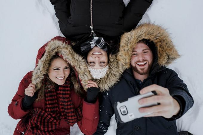 Prieteni cu unghi înalt făcând selfie în timp ce stau întinși pe un câmp acoperit cu zăpadă