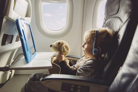 Băiețelul care stă într-un avion urmărind ceva pe tableta digitală