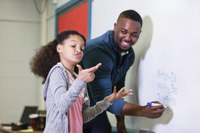 o fată multirasială de 9 ani la ora de matematică, stând la tablă cu profesorul ei, un tânăr afro-american în el 20 de ani, profesorul se uită la elevul său elementar, așteaptă în timp ce ea încearcă să descopere răspunsul, accentul este pus pe fată