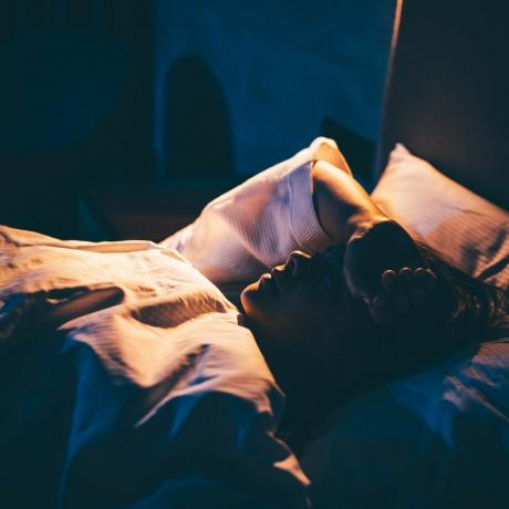 femeie cu insomnie tânără întinsă pe pat cu mâna pe frunte