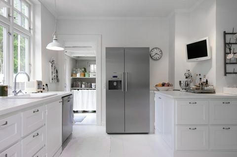 Bucătărie albă cu frigider vertical în argint în renovarea casei Hanne Davidsen, Silkesborg, Danemarca.