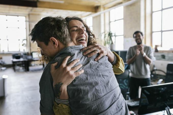 oameni dintr-un spațiu de afaceri startup care sărbătoresc o femeie coleg sunt îmbrățișați de unul dintre colegele ei