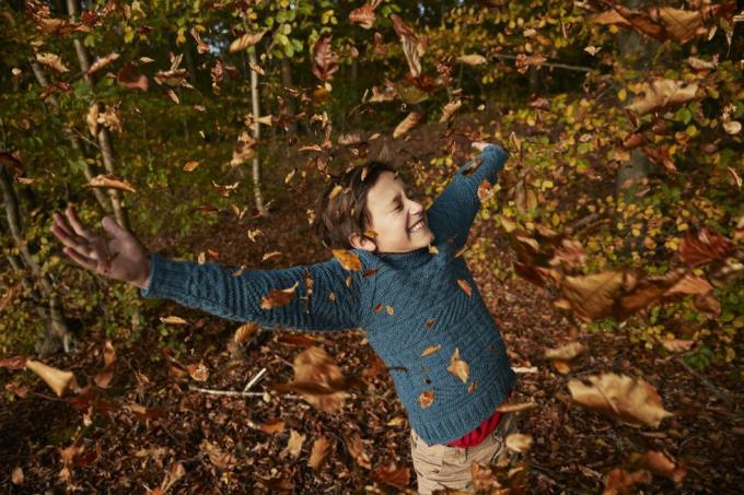 băiat vesel bucurându-se în mijlocul frunzelor de toamnă care cad