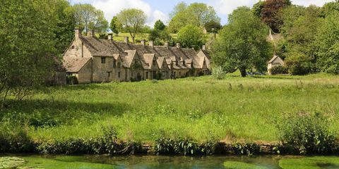 Vedere din Bibury, Gloucestershire, cu pajiști de apă în prim-plan și căsuțe de luturi din lățari în spatele