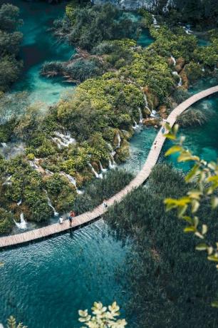 oamenii merg pe cărarea de lemn peste lacuri de-a lungul cascadelor și copacilor din parcul național al lacurilor Plitvice