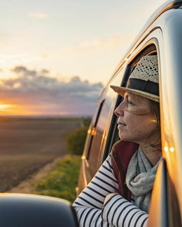 o femeie de 40 de ani admira peisajul rural din rulota ei pare multumita si relaxata